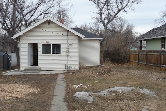 rear view of property featuring entry steps, roof with shingles, a chimney, and fence