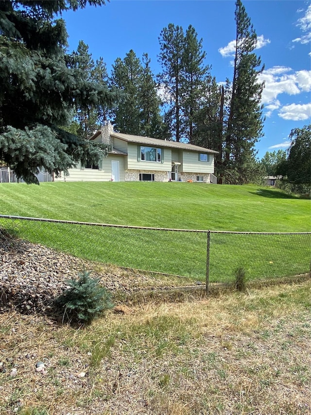 view of front facade featuring stone siding, a front lawn, and fence