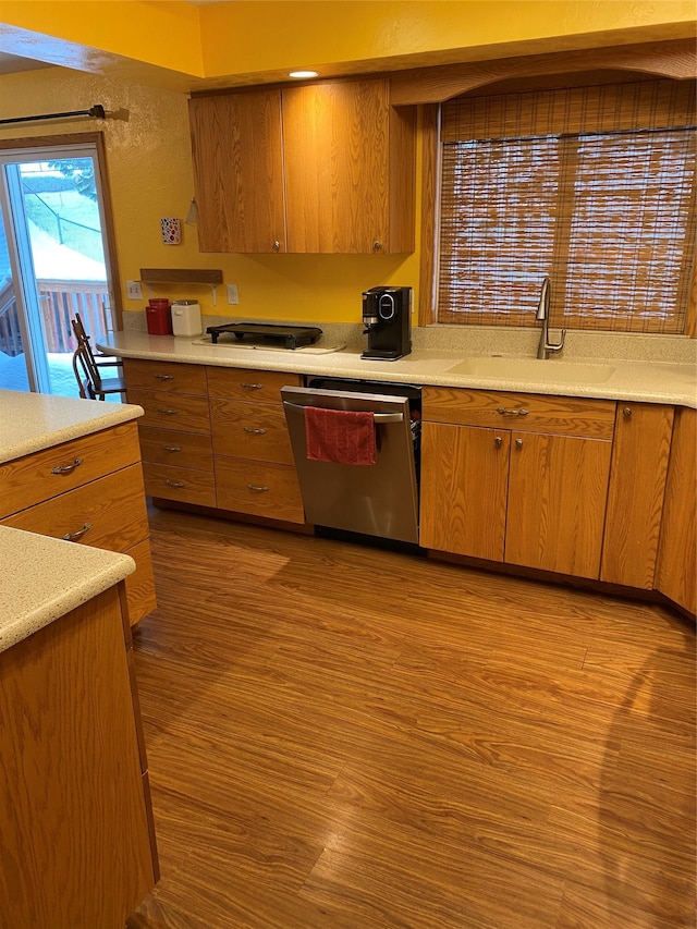 kitchen featuring light wood finished floors, light countertops, stainless steel dishwasher, brown cabinetry, and a sink