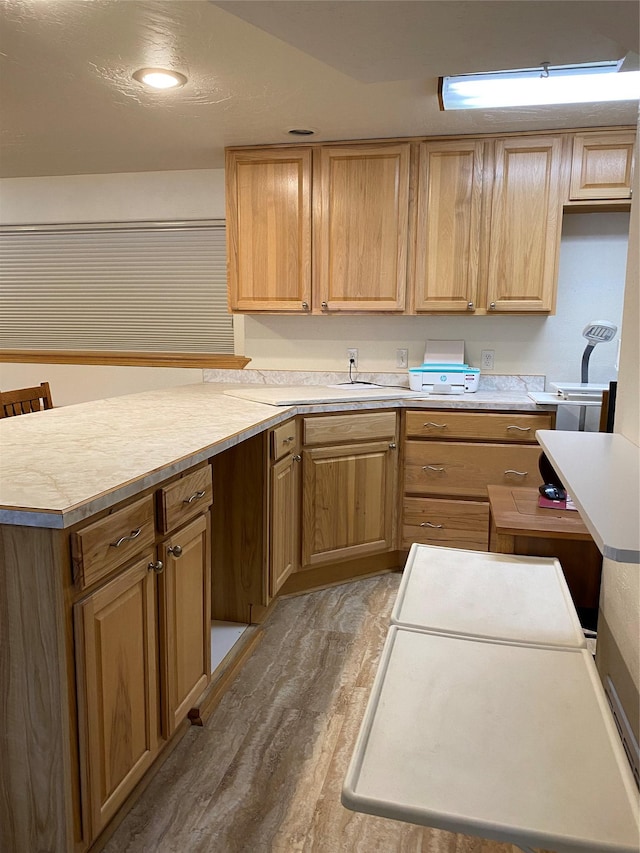 kitchen featuring light countertops, a peninsula, light wood finished floors, and light brown cabinetry