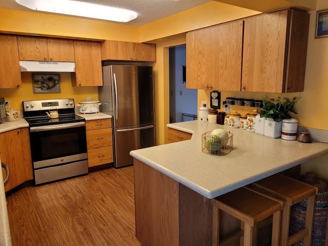 kitchen with light countertops, appliances with stainless steel finishes, a peninsula, under cabinet range hood, and a kitchen breakfast bar