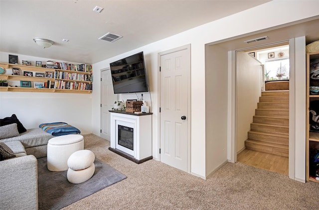 living area featuring a glass covered fireplace, stairway, carpet flooring, and visible vents