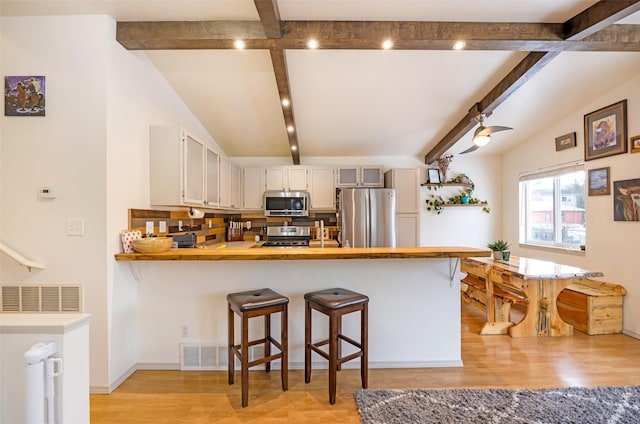 kitchen with vaulted ceiling with beams, light wood-style flooring, a peninsula, light countertops, and appliances with stainless steel finishes