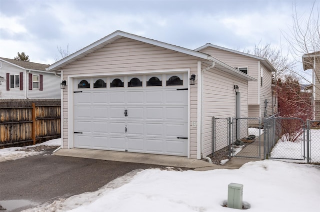 snow covered garage featuring fence and a gate