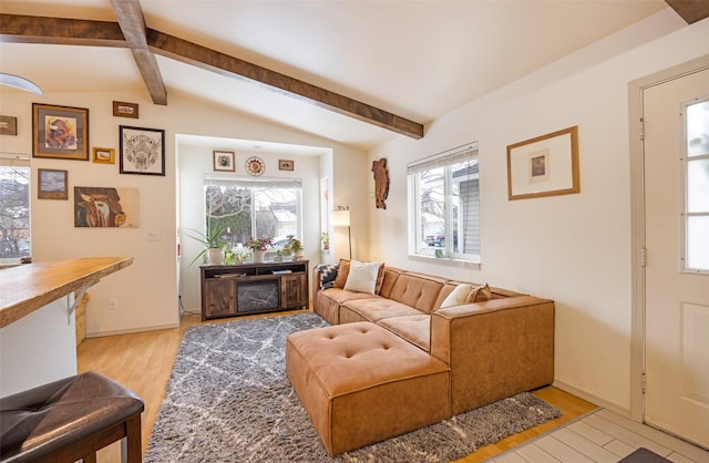 living area featuring vaulted ceiling with beams, light wood-style flooring, and baseboards