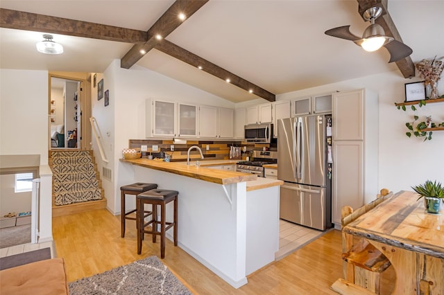 kitchen featuring a breakfast bar area, light wood-style flooring, a peninsula, appliances with stainless steel finishes, and glass insert cabinets