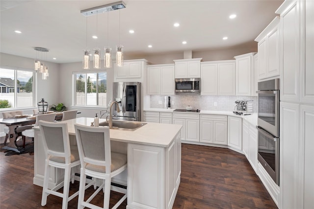 kitchen featuring stainless steel appliances, a sink, light countertops, decorative backsplash, and an island with sink