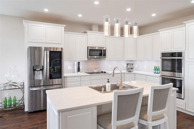 kitchen featuring stainless steel appliances, a sink, backsplash, and a center island with sink