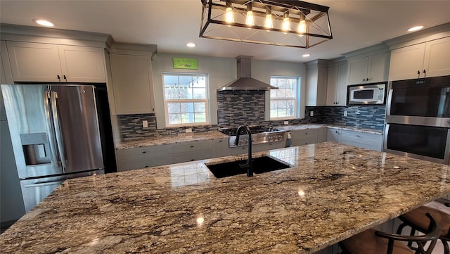 kitchen featuring appliances with stainless steel finishes, a sink, decorative backsplash, and wall chimney exhaust hood