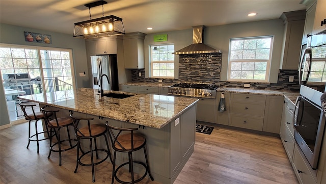 kitchen featuring decorative backsplash, wall chimney exhaust hood, light stone counters, stainless steel appliances, and a sink