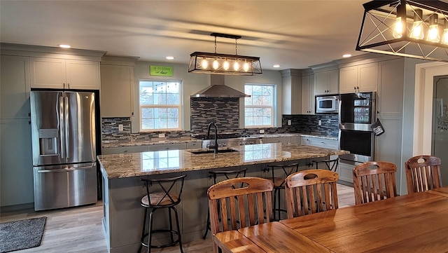 kitchen with stainless steel appliances, wall chimney exhaust hood, a sink, and a kitchen breakfast bar