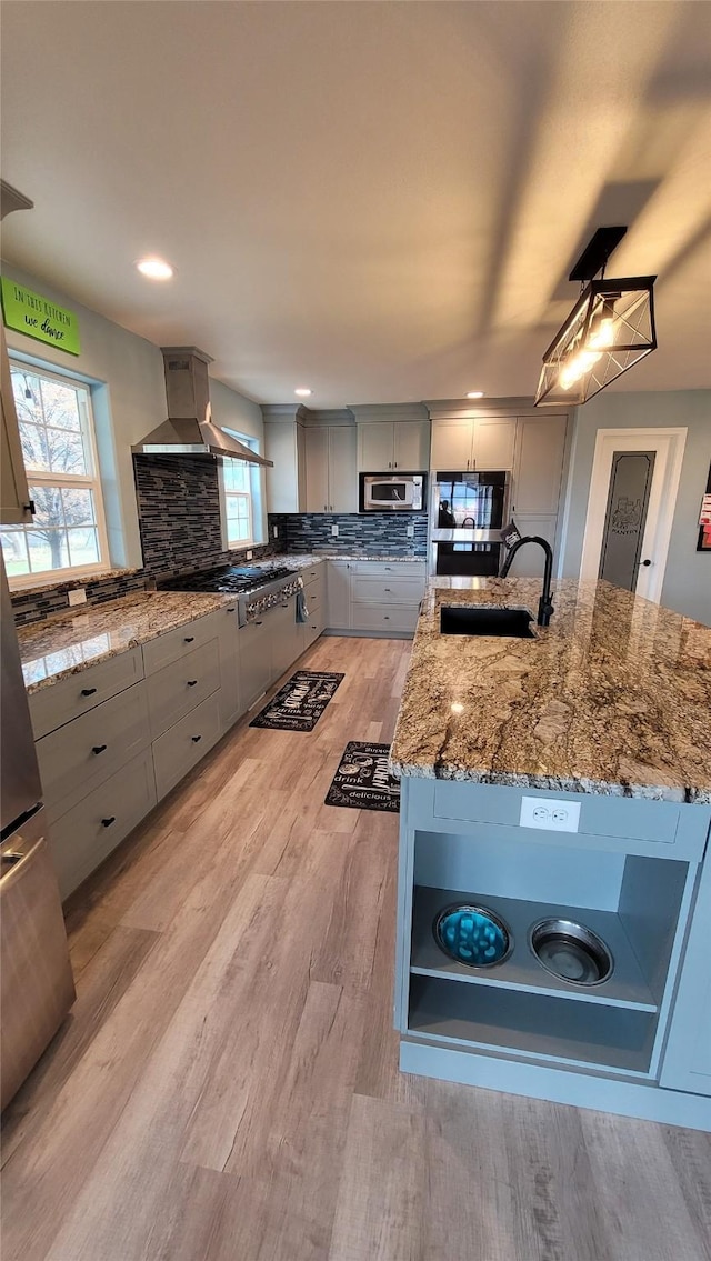 kitchen featuring a sink, wall chimney range hood, appliances with stainless steel finishes, gray cabinets, and backsplash