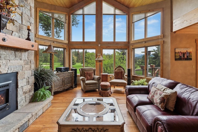 living room with a stone fireplace, wooden ceiling, wood finished floors, and a towering ceiling