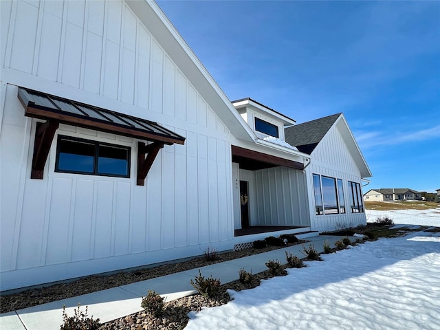 snow covered property with a shingled roof, a standing seam roof, and board and batten siding