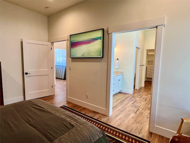 unfurnished bedroom featuring ensuite bath, light wood-style flooring, and baseboards