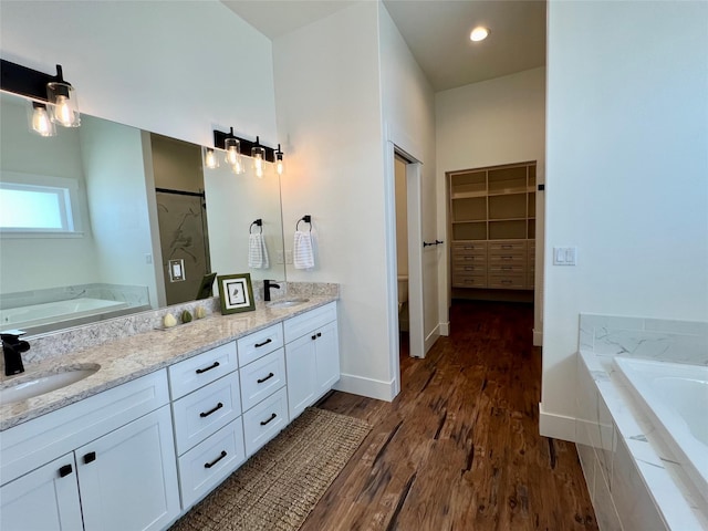 bathroom featuring double vanity, a bath, a sink, and wood finished floors