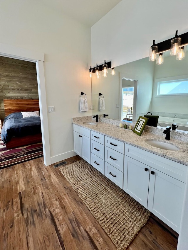 ensuite bathroom with double vanity, wood finished floors, a sink, and connected bathroom