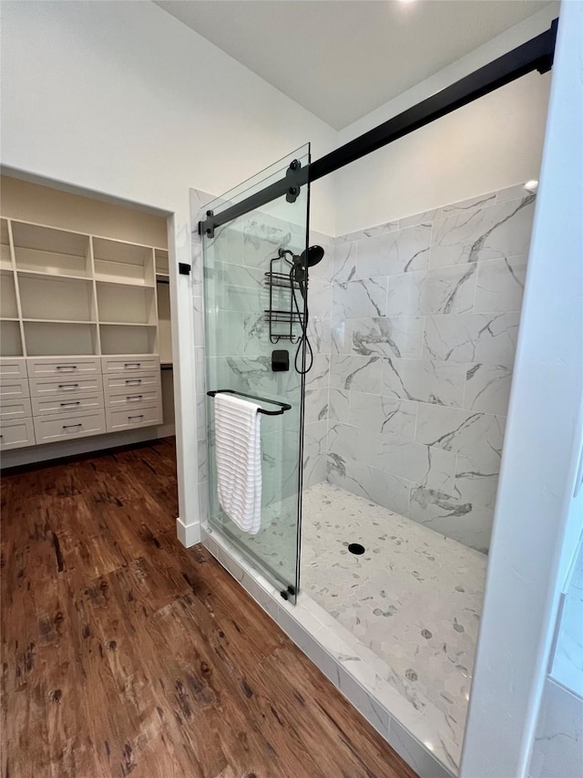 bathroom featuring a spacious closet, wood finished floors, and a marble finish shower