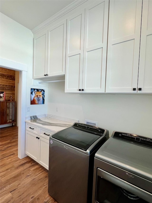 clothes washing area with light wood finished floors, washing machine and clothes dryer, and cabinet space