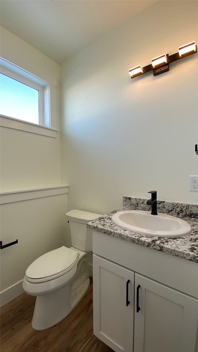 half bathroom with toilet, wood finished floors, and vanity