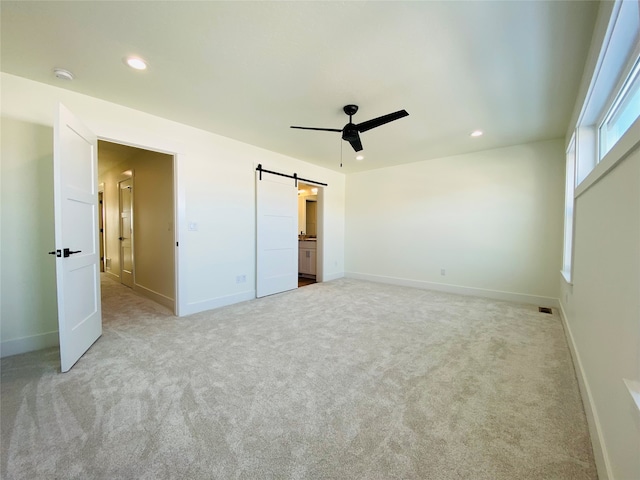 unfurnished bedroom featuring light carpet, a barn door, and recessed lighting