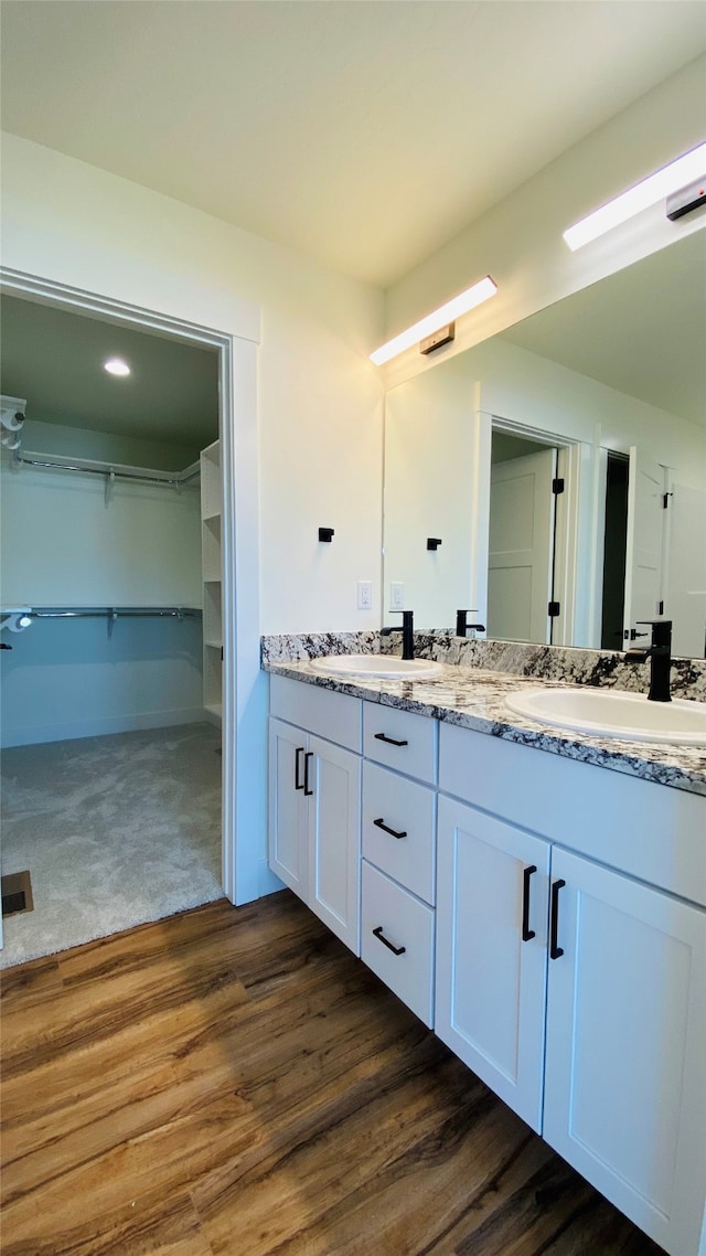 bathroom featuring double vanity, a sink, a spacious closet, and wood finished floors