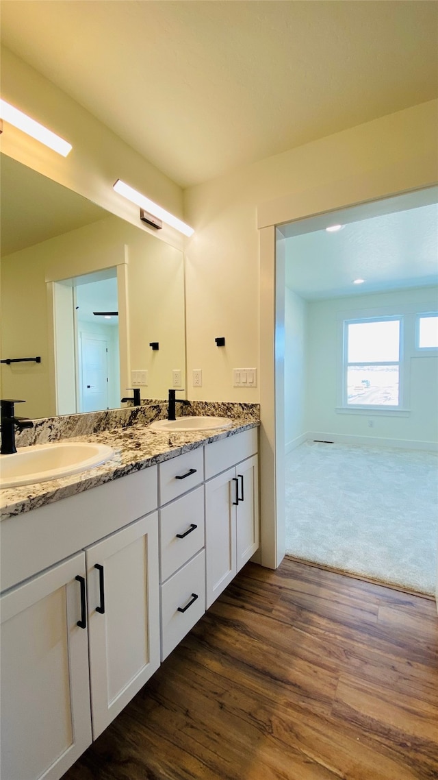 full bath with double vanity, baseboards, a sink, and wood finished floors