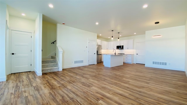 unfurnished living room with stairway, light wood-type flooring, a sink, and visible vents