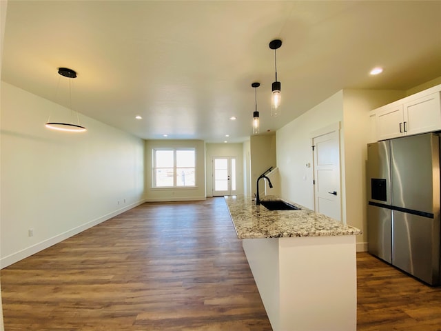 kitchen with dark wood-style floors, hanging light fixtures, a sink, light stone countertops, and stainless steel fridge