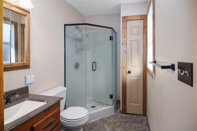 bathroom with stone finish flooring, toilet, a shower stall, and vanity