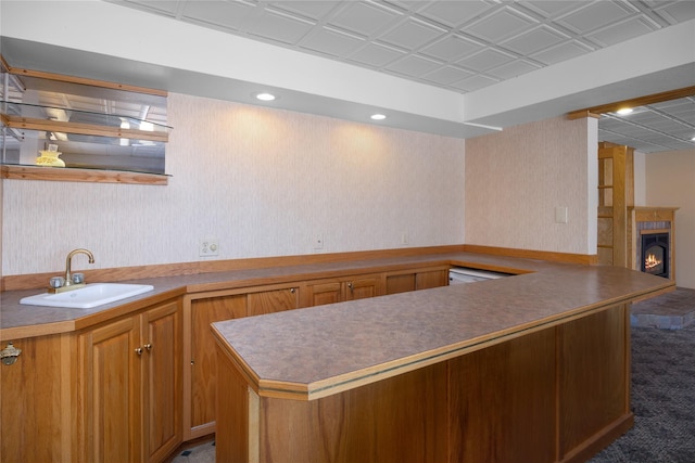 kitchen featuring a sink, a lit fireplace, brown cabinetry, carpet, and wallpapered walls