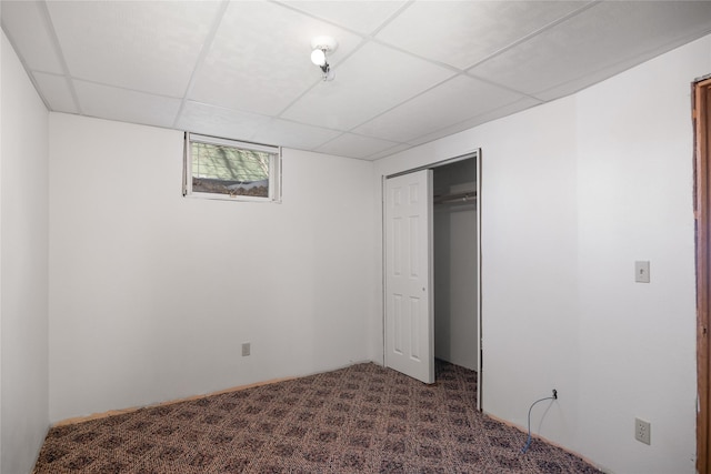 unfurnished bedroom with dark colored carpet, a closet, and a paneled ceiling