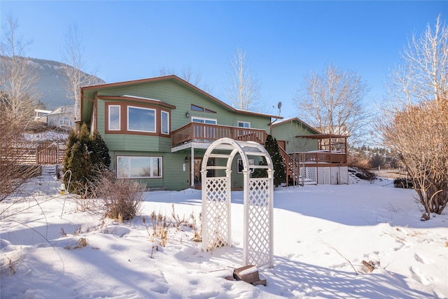 snow covered rear of property with stairs and a wooden deck