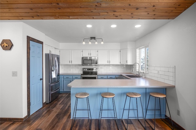 kitchen with dark wood-style flooring, stainless steel appliances, backsplash, a sink, and a peninsula