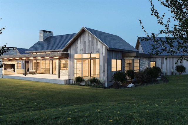 back of property with a standing seam roof, metal roof, a lawn, a chimney, and a patio area