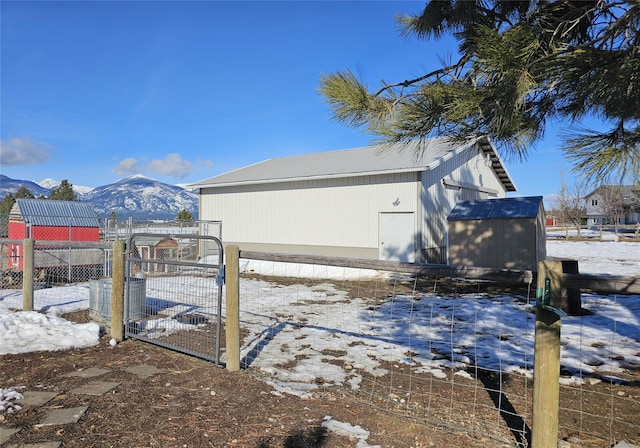 snow covered property featuring a gate, fence, a mountain view, and an outbuilding