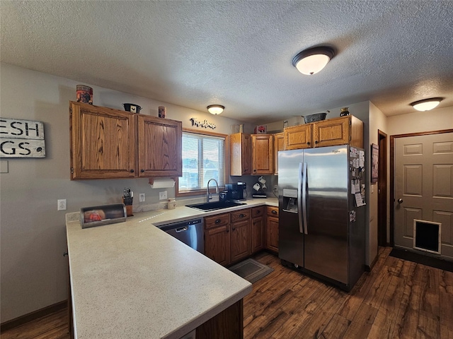 kitchen featuring a peninsula, a sink, light countertops, appliances with stainless steel finishes, and dark wood finished floors