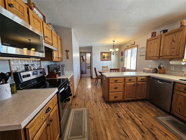 kitchen featuring a peninsula, appliances with stainless steel finishes, dark wood-type flooring, and light countertops