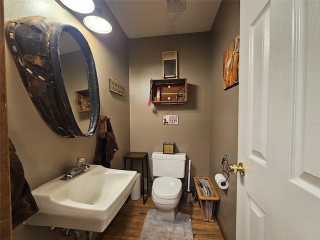 half bathroom featuring toilet, a sink, wood finished floors, and visible vents