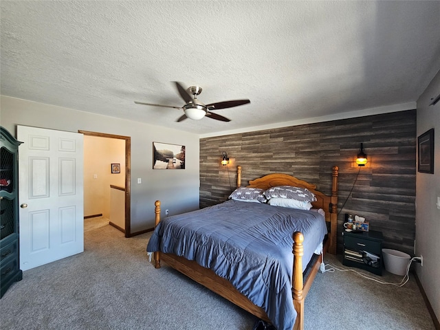 bedroom with carpet, an accent wall, a ceiling fan, wooden walls, and a textured ceiling