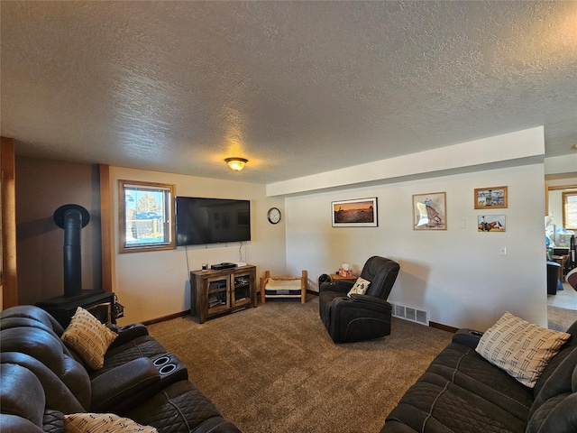 carpeted living room featuring visible vents, a textured ceiling, a wood stove, and baseboards