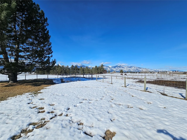 yard layered in snow featuring a mountain view and fence