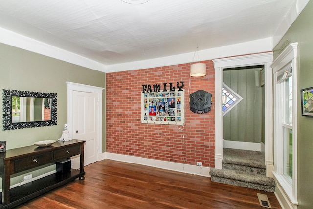 interior space featuring baseboards, visible vents, brick wall, and wood finished floors