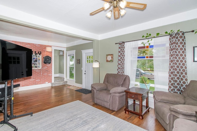 living room featuring ceiling fan, brick wall, wood finished floors, and baseboards