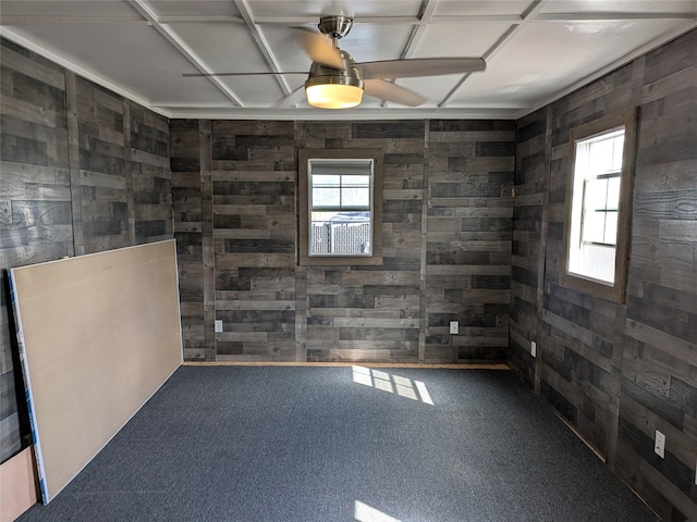 carpeted empty room with a ceiling fan and wooden walls