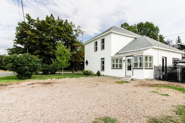 back of property featuring roof with shingles, fence, entry steps, and gravel driveway