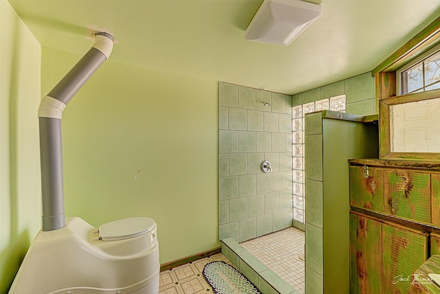 bathroom with tiled shower, toilet, and baseboards