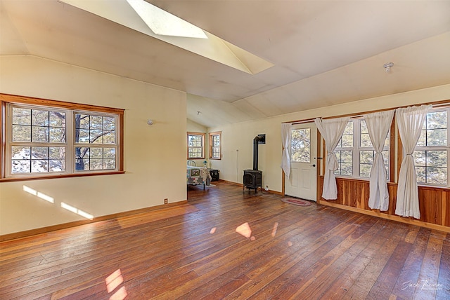 unfurnished room with vaulted ceiling with skylight, wood-type flooring, a wood stove, and baseboards