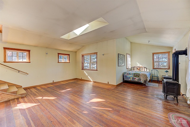 bedroom featuring lofted ceiling with skylight, wood-type flooring, multiple windows, and a wood stove