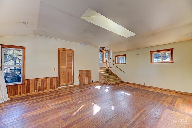 interior space featuring vaulted ceiling with skylight, a wainscoted wall, and hardwood / wood-style flooring